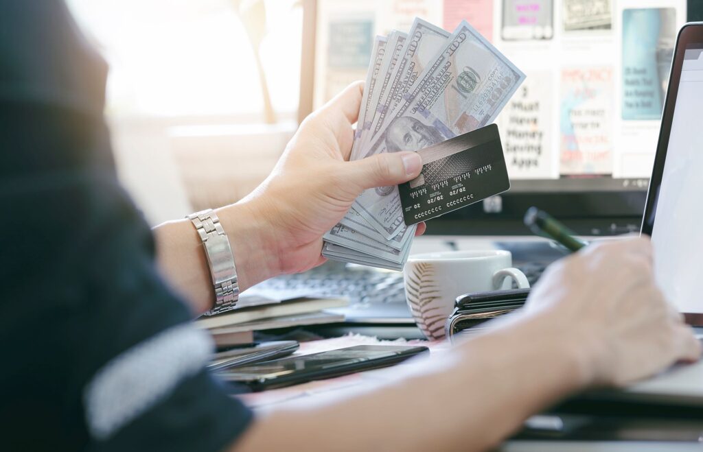 Man holding credit card dollars banknote while using laptop shopping online